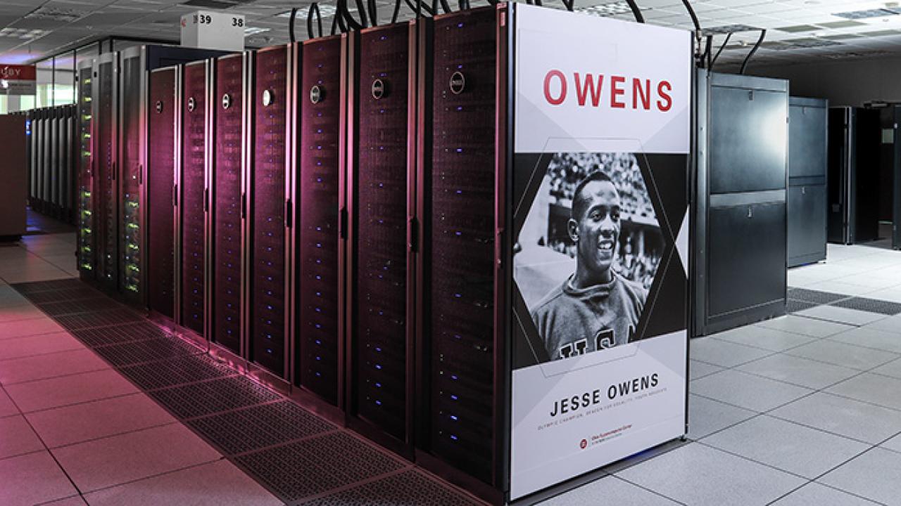 A supercomputer system with large black server cabinets and a display panel showing "OWENS" and an image.