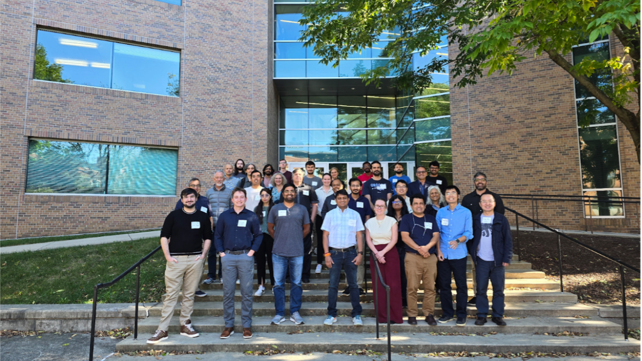 2 rows of people standing in front of a brick building wearing name tags